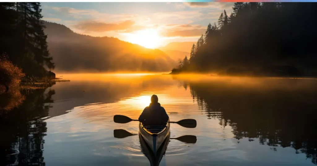 A person kayaking on a calm lake at sunrise, surrounded by mist and mountains.